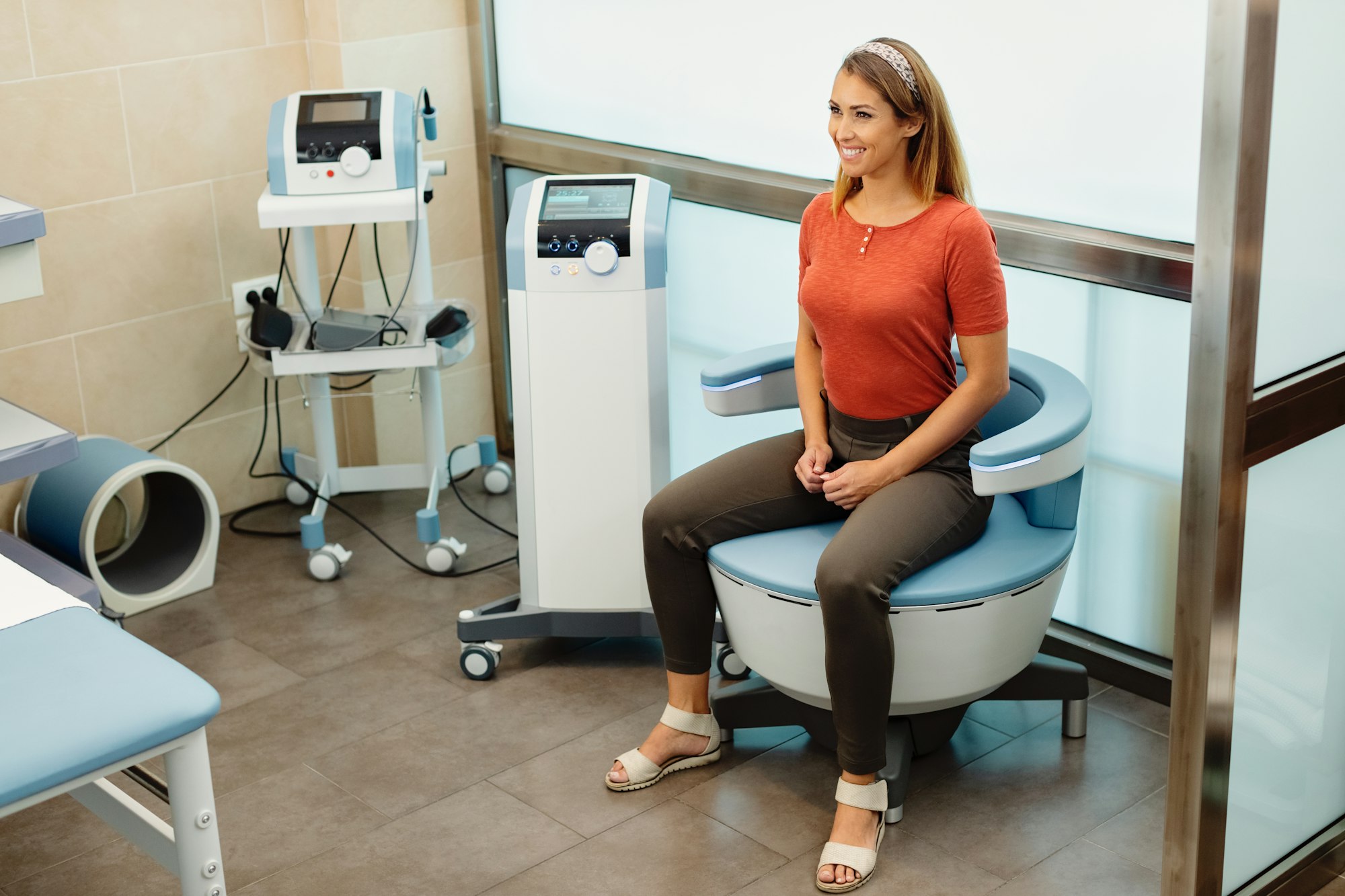 Happy woman during electromagnetic procedure for urinary incontinence at medical clinic.